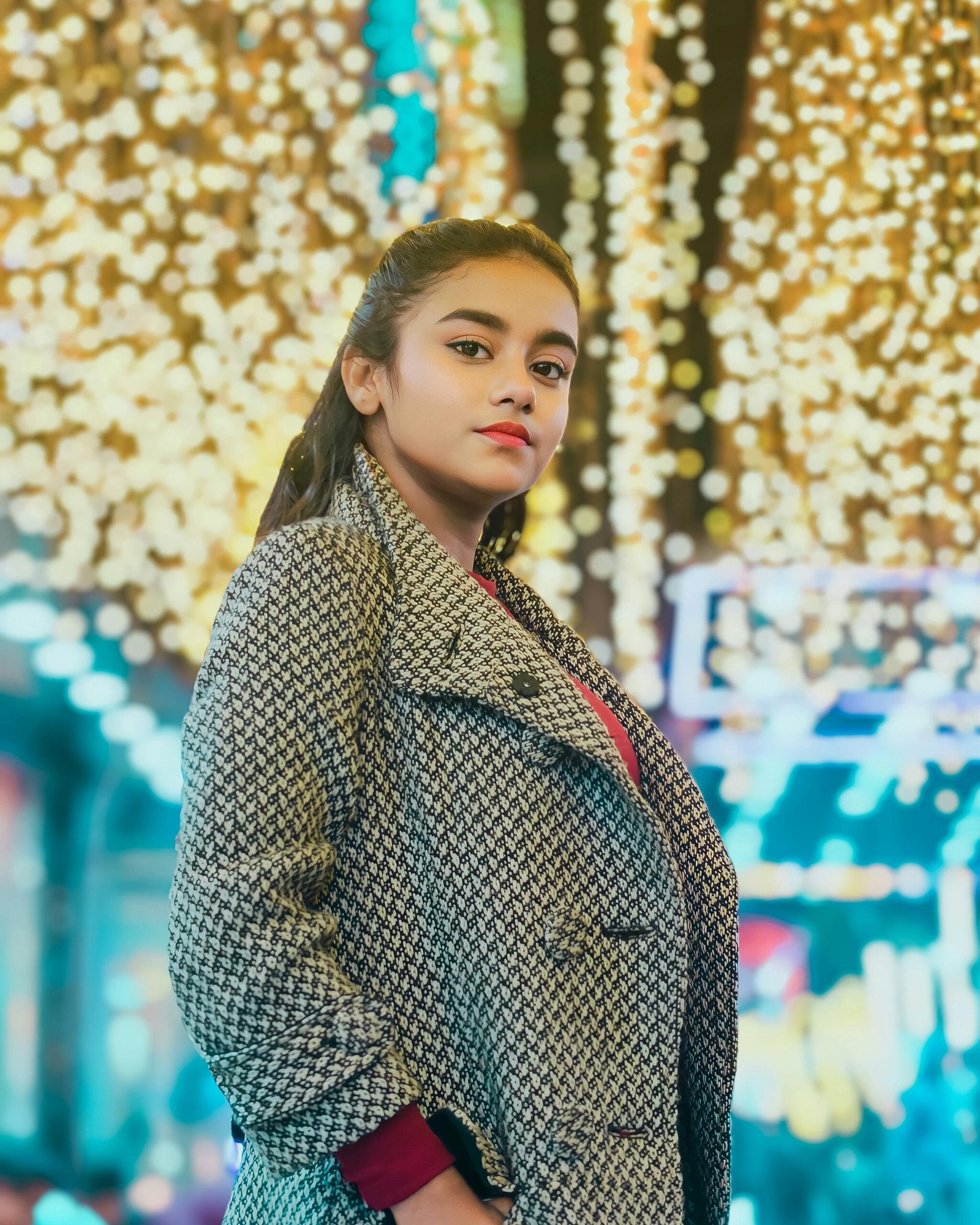 Portrait of a woman in a coat standing on a vibrant city street decorated with festive lights during winter.
