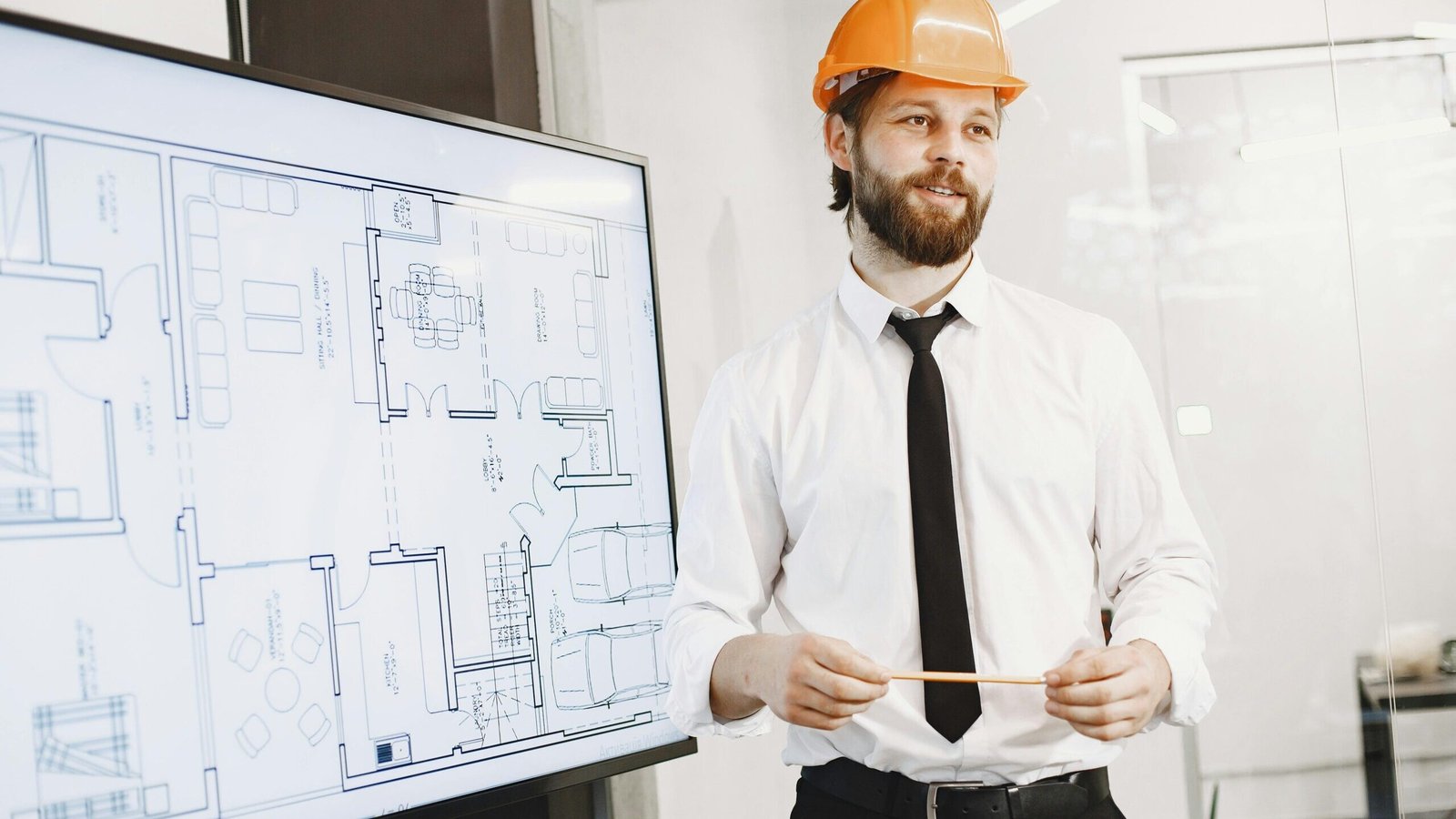 Seohara me Best Architect kaun ho sakta hai? | Architect in orange helmet presenting building blueprints in a modern office setting. Professional and confident.