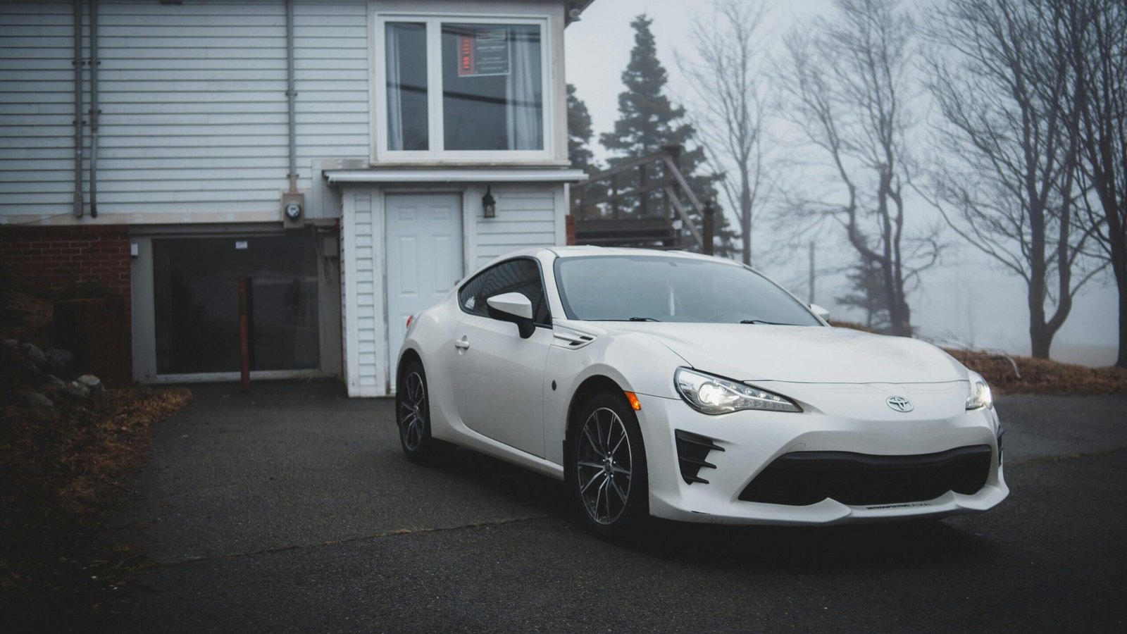 Modern white sport automobile parked on asphalt road near garage of cottage in countryside