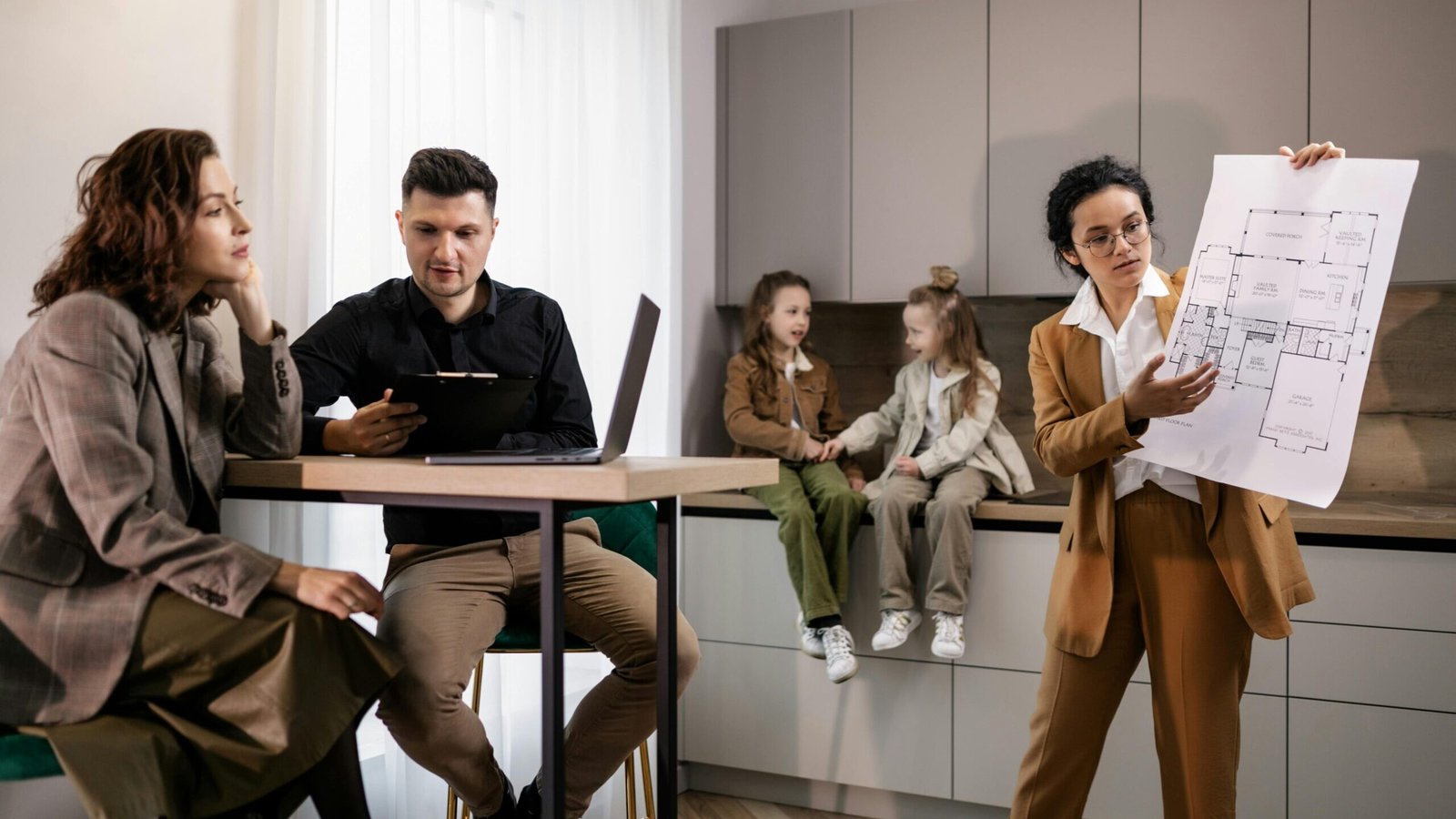 Real estate agent presenting house plans to clients in a modern kitchen setting.