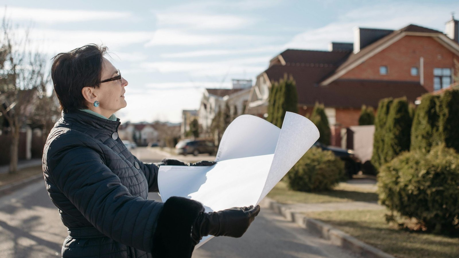घर का नक्शा बनवाते समय क्या ध्यान रखें | Woman in a blue jacket reviewing architectural plans outdoors on a sunny day.