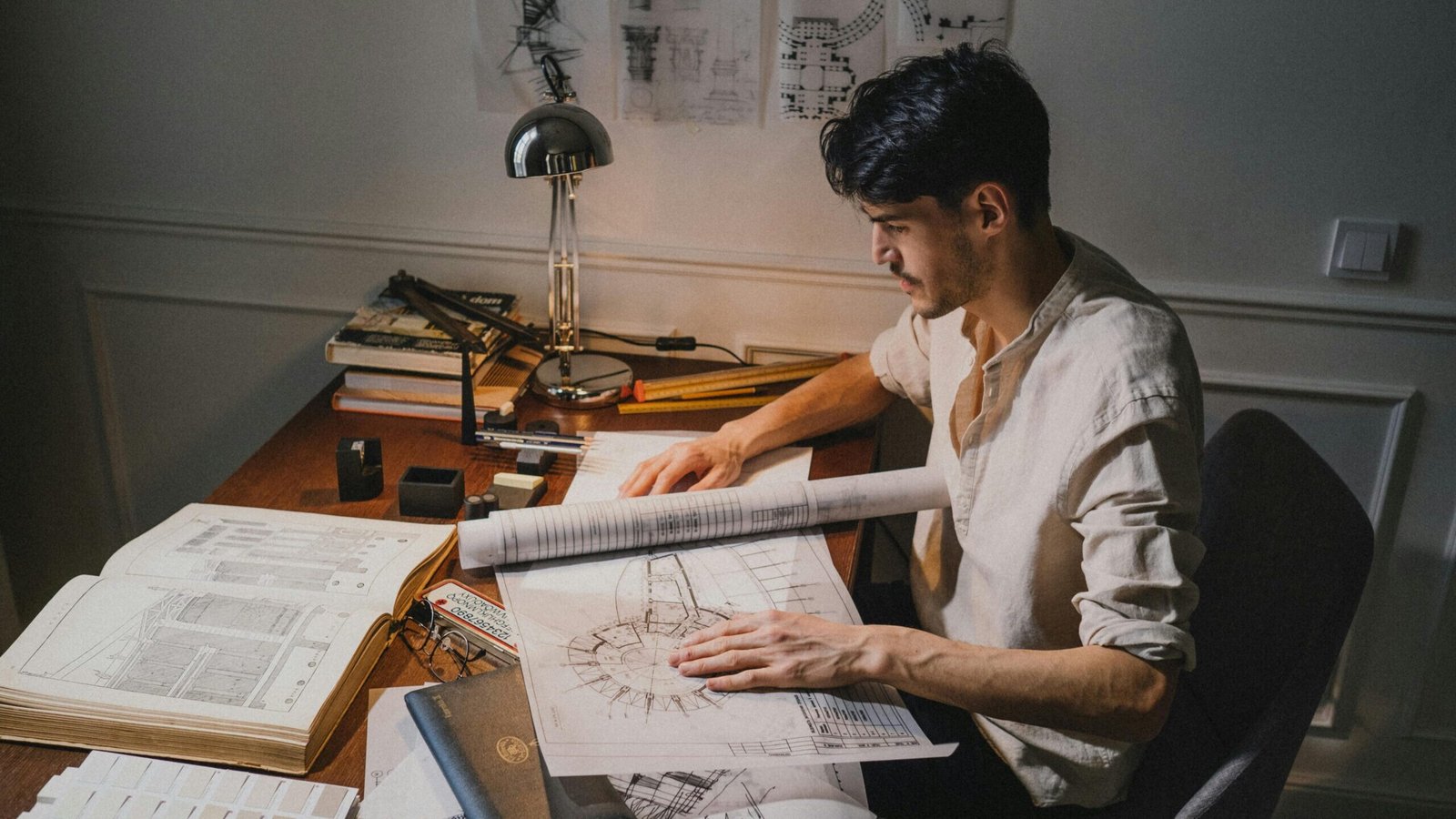 District Bijnor me Top Civil Engineer & Architect kaise milega? | Young architect at a desk working on blueprint designs under lamp light.